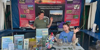 Two women at a conservation booth with educational displays and a prize wheel.