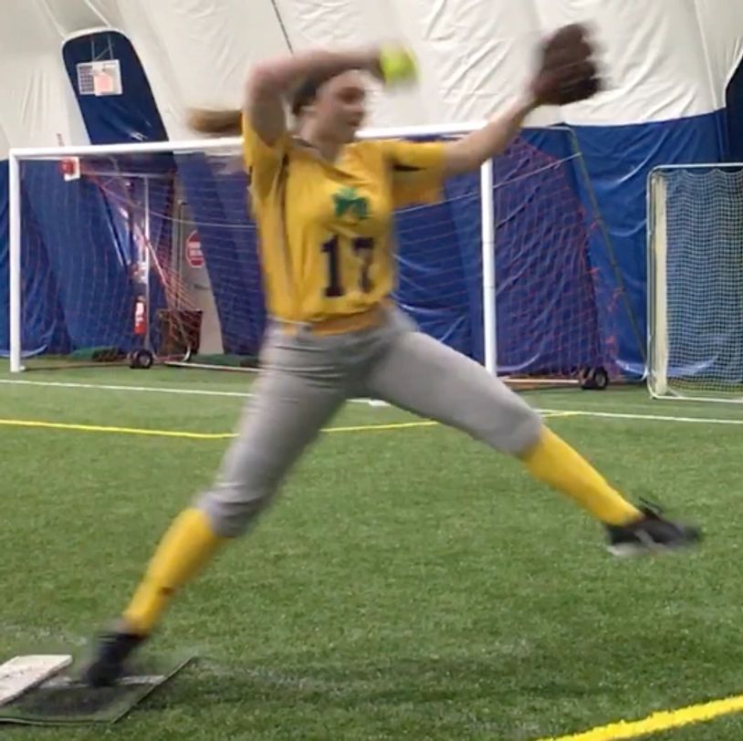 Softball pitcher mid-pitch indoors.