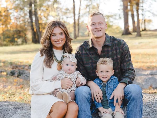A happy family of four posing outdoors on a rock in autumn.