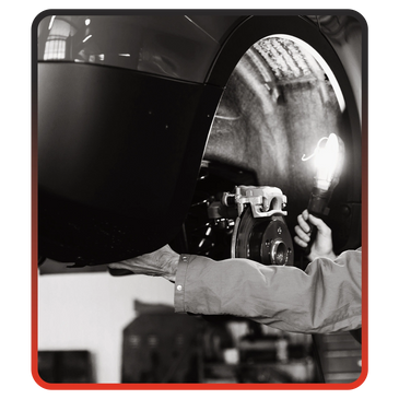 Mechanic inspecting a car brake system with a flashlight in a garage.