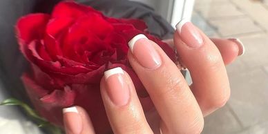 Hand with French manicured nails holding a red rose.