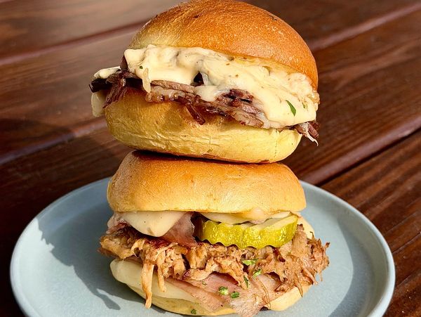 Two stacked pulled pork sandwiches with melted cheese and pickles on a plate.