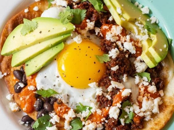 Huevos rancheros with avocado, ground meat, black beans, and cheese on a tortilla.