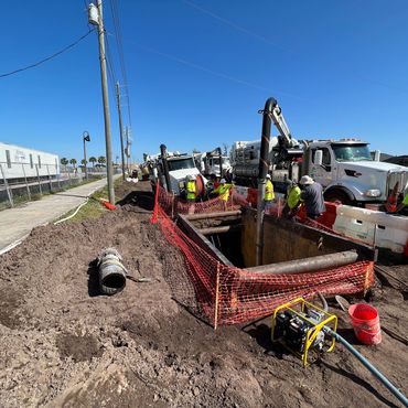 Construction workers operating near a large trench and trucks on a sunny day.