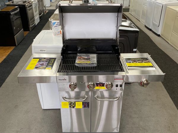 A new stainless steel BBQ with advertising stickers in a row of used appliances.
