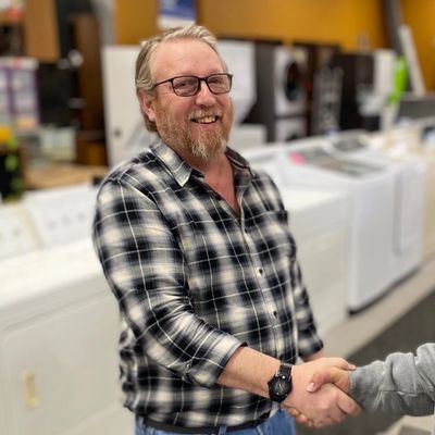 A businessman is smiling and shaking a hand in front of a row of appliances.