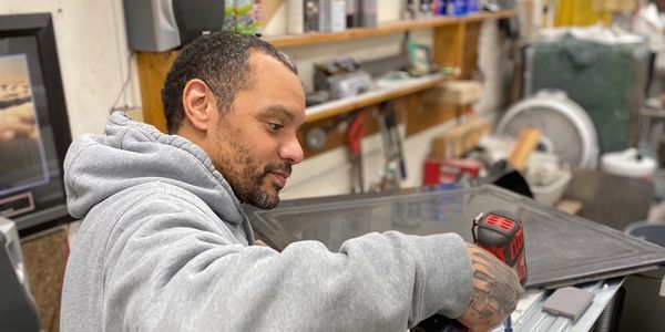 A repairman working on a refrigerator using a drill gun.