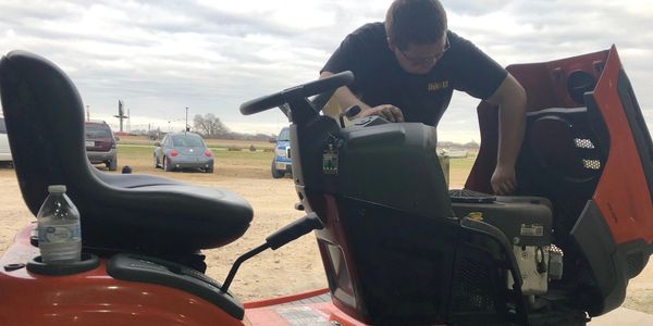 Mechanic repairing an orange riding lawn mower.