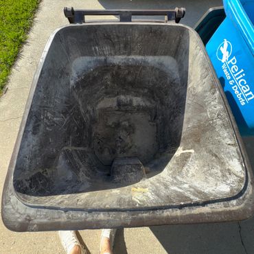 Empty trash bin ready for collection near a waste service truck and recycling bin.