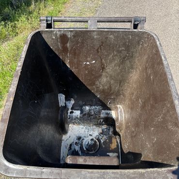 Empty brown trash bin outdoors on a sunny day.