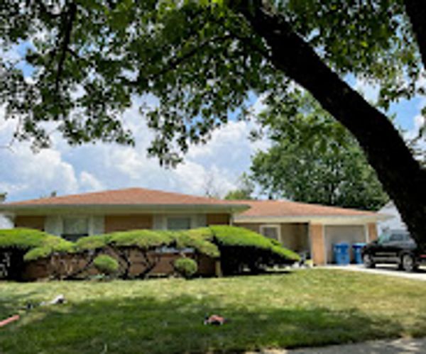 A single-story house with a brown roof, surrounded by greenery and trees.