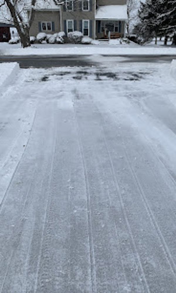 A snowy driveway leading to a cleared street in a residential area.