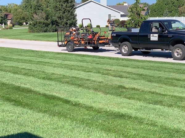 A pickup truck towing a trailer with lawn equipment near a freshly mowed lawn.
