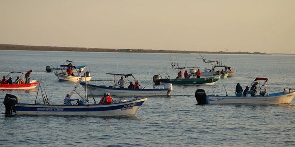 Several fishing boats with people on calm water during sunset.