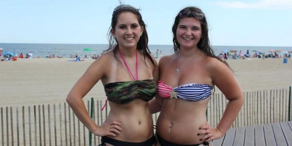 Two women smiling in swimsuits on a beach boardwalk.