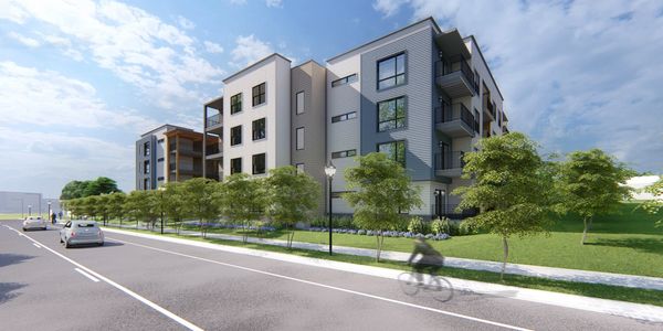 Modern apartment buildings with trees and a cyclist on the road.