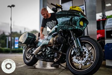 Man cleaning a custom motorcycle at a gas station.