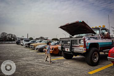 Boy looking at an old truck with open hood in a parking lot.