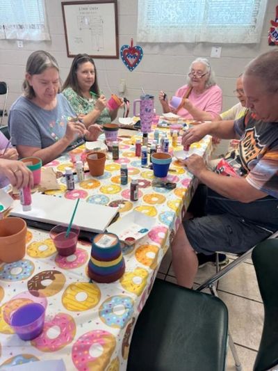 Group of adults painting flower pots together at a colorful donut-themed table.