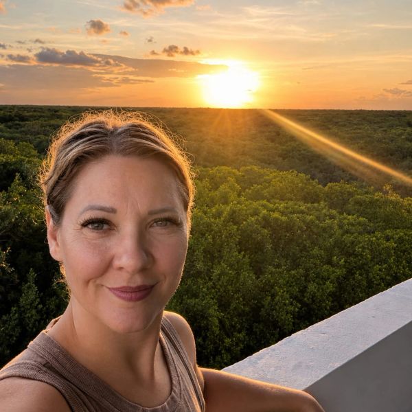 Woman taking a selfie with a sunset and forest background.