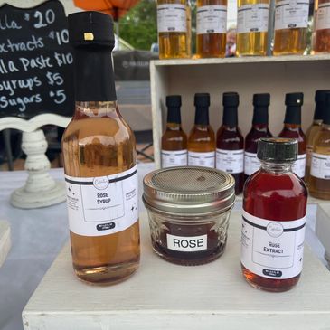 Bottles and jars of rose extract and syrup displayed at a market stall.