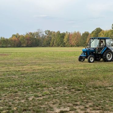 A tractor mowing a large grassy field near a tree line.