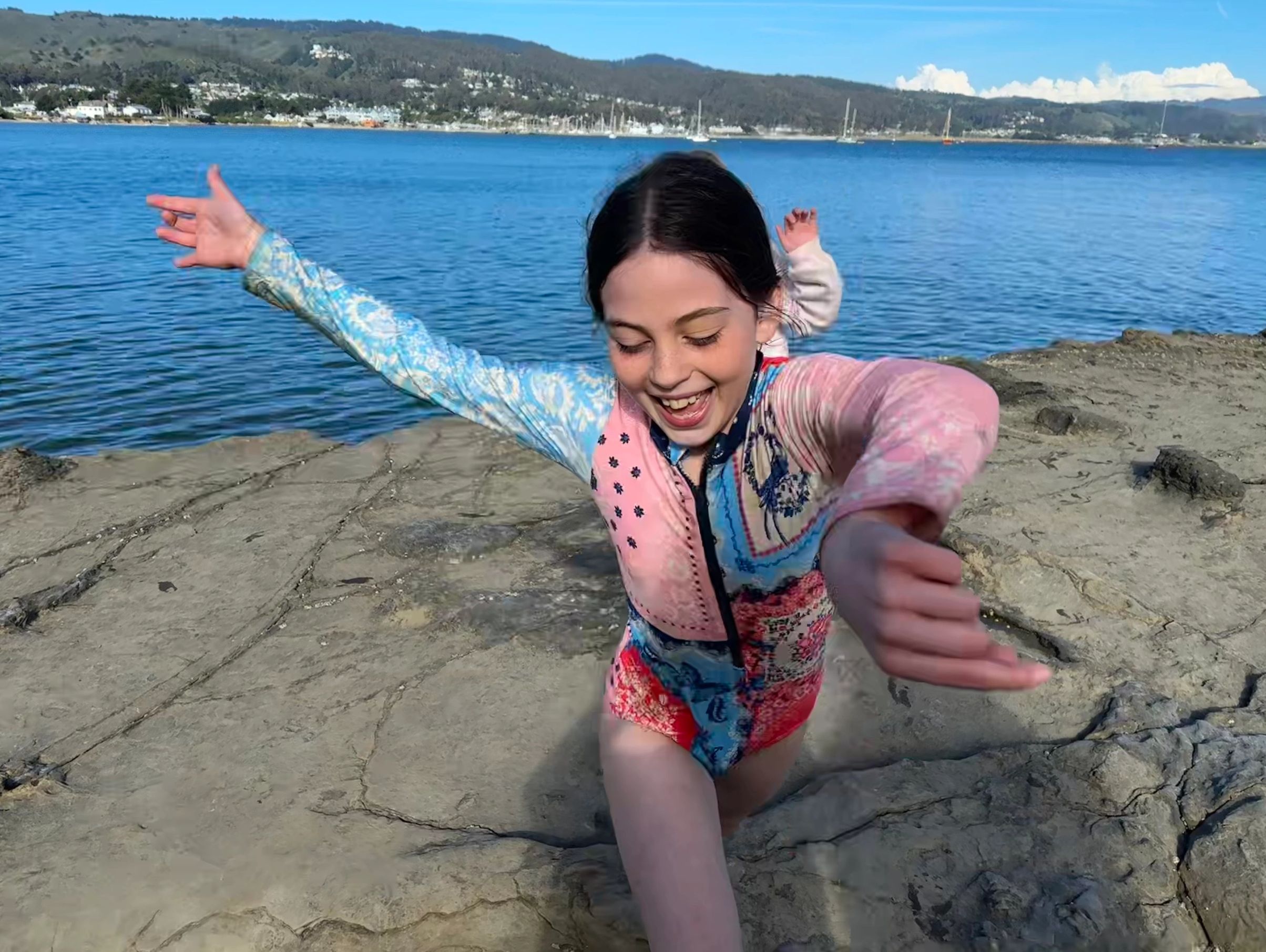 A joyful girl with arms outstretched near a scenic waterfront.