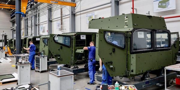 Workers assembling military vehicle cabins inside a factory.