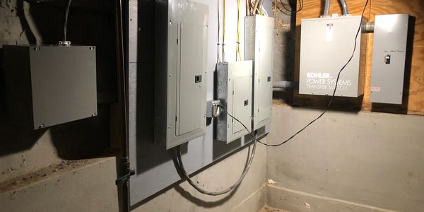 A basement wall with multiple electrical panels and cables installed.