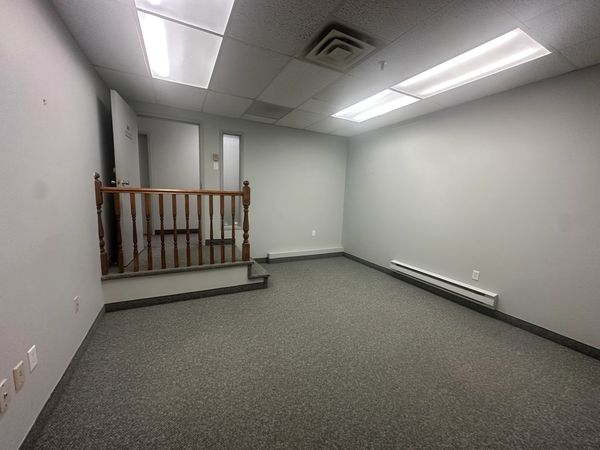 Empty office room with gray walls and carpet, fluorescent ceiling lights, and a wooden railing.
