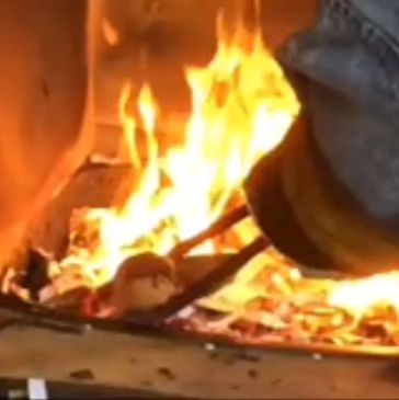 Raku process showing art ceramic piece being added to fire blazing reduction bin. 