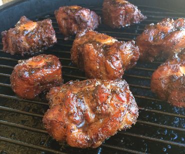 Grilled, seasoned meat pieces cooking on a barbecue grill.