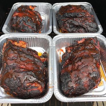 Four trays of smoked, sauced meats with a charred crust.