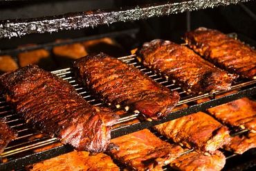 Tender ribs slow-cooking on a smoker rack, rich with barbecue sauce.