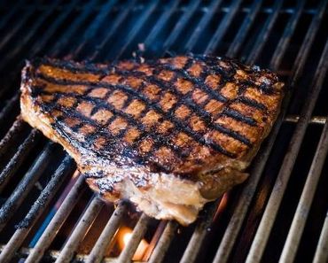 Grilled steak with char marks cooking on a barbecue grill.