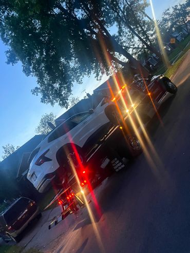 A white car is being towed on a flatbed truck during dusk.