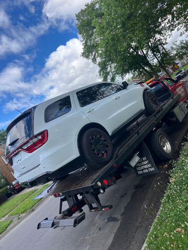 White SUV being towed on a flatbed truck on a suburban street.