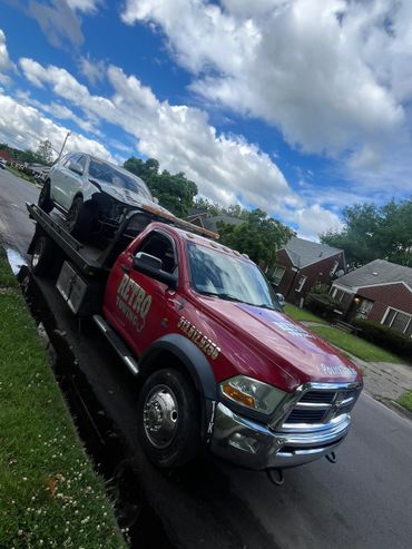 A red Retro Towing truck carrying a damaged silver car on a suburban street.