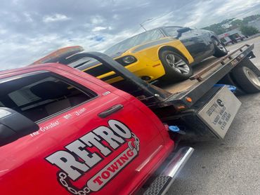 A yellow and black car is being towed on a red Retro Towing truck under a cloudy sky.
