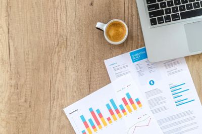 Workspace with a laptop, coffee, and colorful charts on a wooden table.