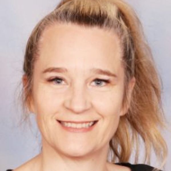 Smiling woman with blonde hair tied in a ponytail against a plain background.