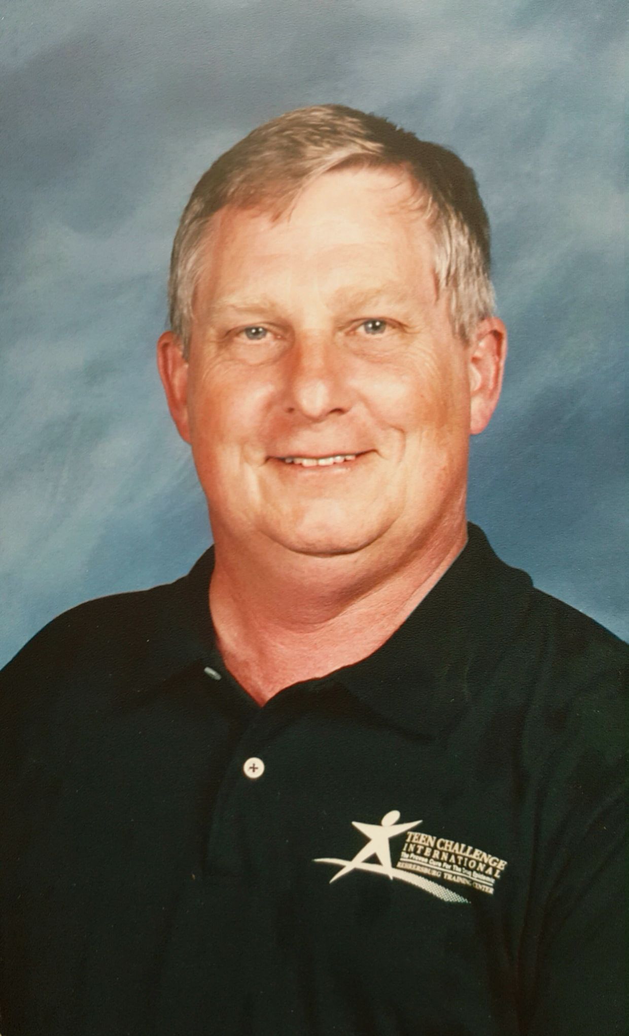 Middle-aged man smiling in a black polo shirt.