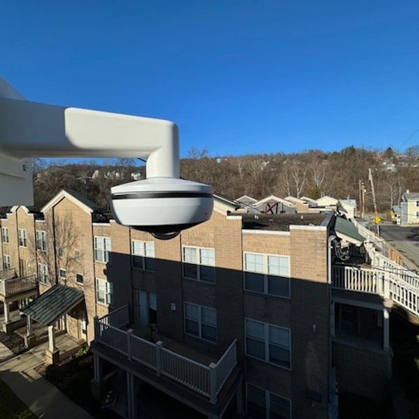 Security camera mounted outside overlooking residential buildings on a sunny day.