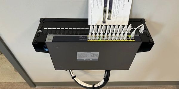 Wall-mounted network switch with multiple connected Ethernet cables and a guide on top.