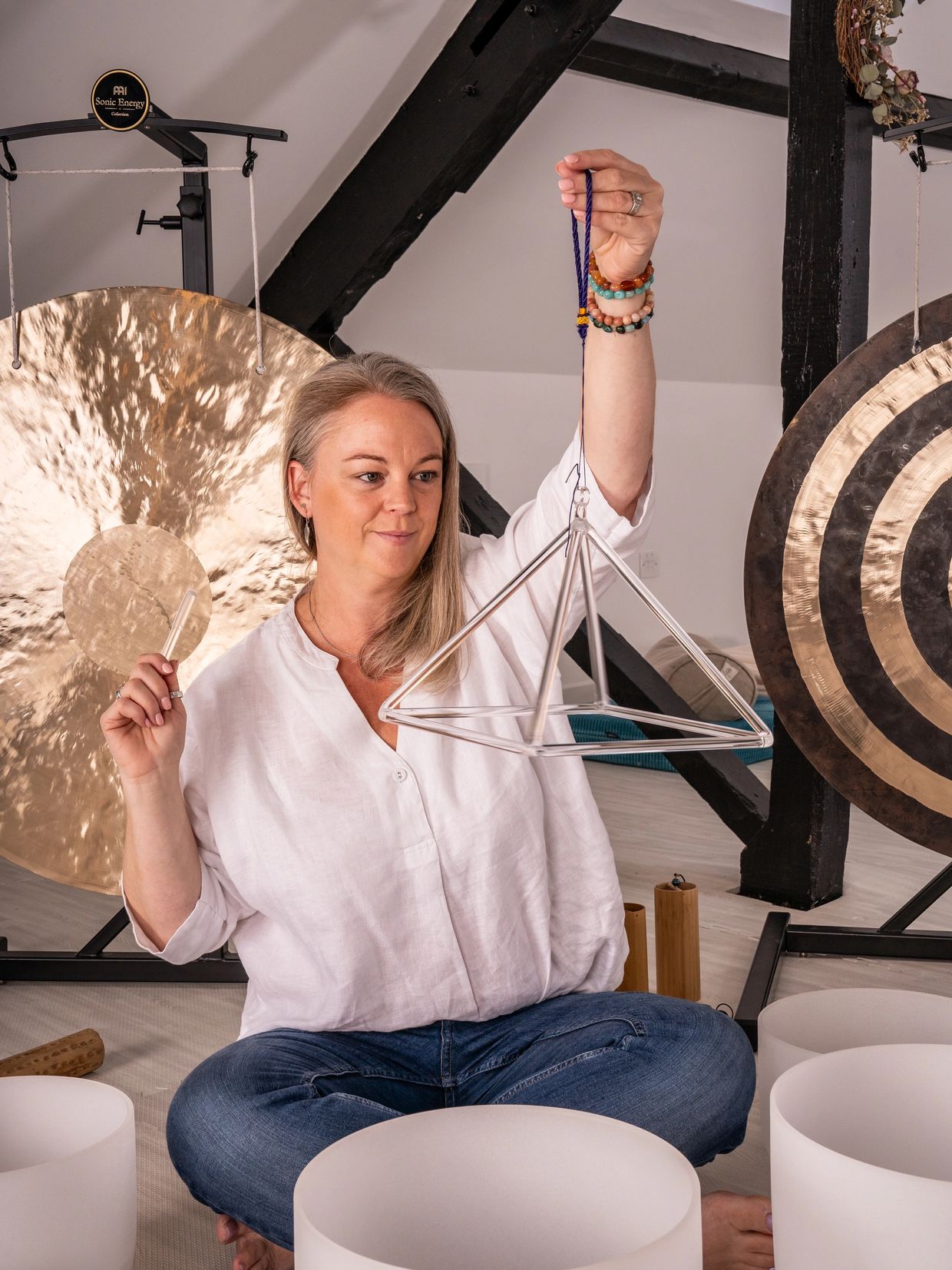 Woman playing a triangle with gongs in the background.