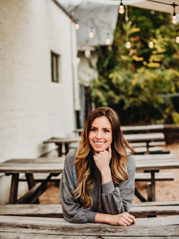 Smiling woman leaning on a wooden picnic table outdoors.