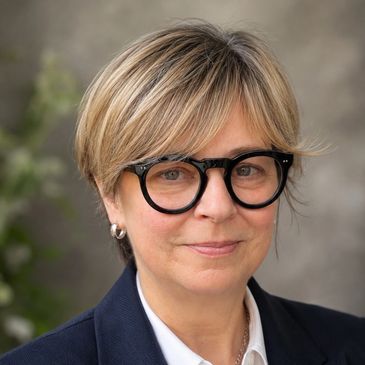 Woman with short blonde hair wearing large black glasses.