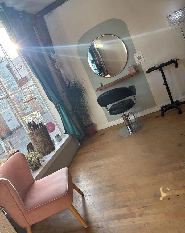 Bright hair salon corner with a pink chair and black styling chair.