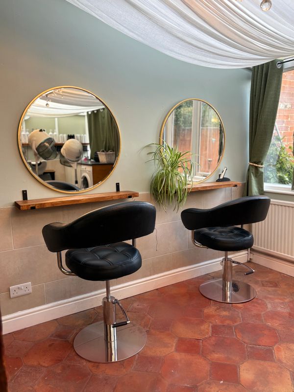 A cozy salon space with two black chairs and round mirrors.