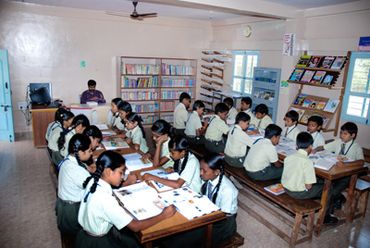 Students in green uniforms reading books in a school library.